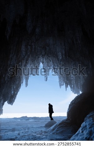 Person exploring inside of a cave with the ceiling full of icicles during winter, Lake Superior 