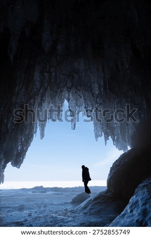 Person exploring inside of a cave with the ceiling full of icicles during winter, Lake Superior 