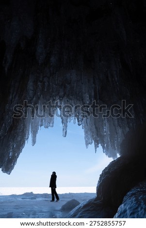 Person exploring inside of a cave with the ceiling full of icicles during winter, Lake Superior 