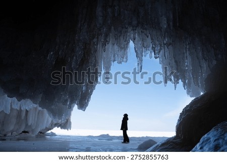 Person exploring inside of a cave with the ceiling full of icicles during winter, Lake Superior 
