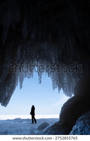 Person exploring inside of a cave with the ceiling full of icicles during winter, Lake Superior 
