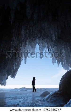 Person exploring inside of a cave with the ceiling full of icicles during winter, Lake Superior 