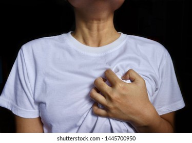 Person expressed pain by grasping hard on chest, stands in black background