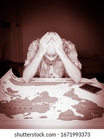 Person With Face Mask And Hand On His Head Looks Concerned To The World Paper Map  With Passport On It. Concept Of Warning And Cancelled Travel Plans Cause Of Sickness And Covid-19 Virus.