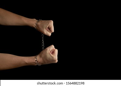 Person With Fetters On Hands Isolated On A Black Background With Copy Space. Breaking Chains Concept. Dark Minimal Mood. 