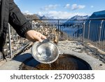 A person filling a bowl with water at a fountain on Monte Bre, Switzerland, overlooking the Alps