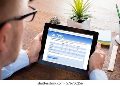 Person Filling Online Survey Form On Digital Tablet At Wooden Desk