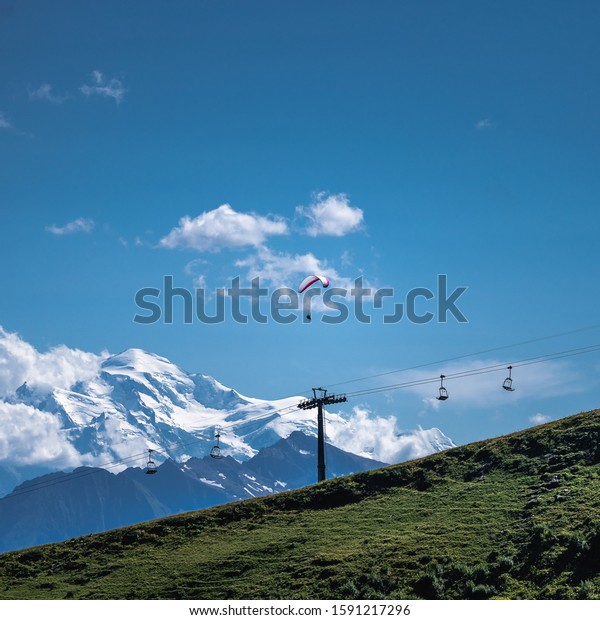 A person flying a parachute over a\
ropeway surrounded by a mountainous\
scenery