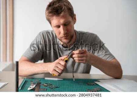 A person is focused on using a pcb knife to work on a circuit board on a worktable during the afternoon.