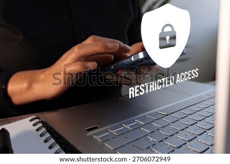 A person in front of a computer while using a cell phone with restricted access icons.