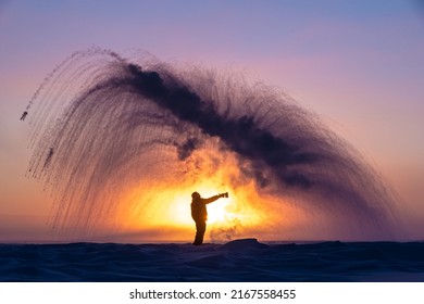 Person In Full Winter Clothing Throws A Pitcher Of Boiling Water Into The Air, Creating Rapid Freezing At Arctic Temperature.