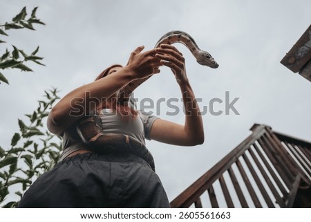 A person gently holding a snake while standing outside on a cloudy day. The scene conveys connection with nature and adventure, highlighting the intrigue of wildlife interaction.