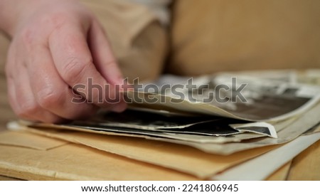Person grabs and examines carefully old photos from vintage album. Owner enjoys remembering amazing moments looking through faded photos, closeup