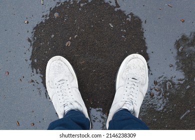 Person in gray boots standing on pavement wet after rain, top view. Close-up of legs in shoes, pov.