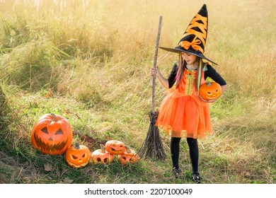 A person in the guise of a witch with a broomstick in her hand looks down at a lot of carved scary and evil pumpkins on Halloween day. - Shutterstock ID 2207100049