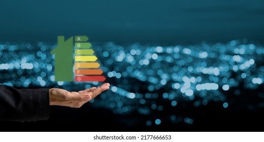 Person hand and house icon with energy efficiency scale image on blue bokeh background, Concept of ecological and bio energetic house. Energy class. - Shutterstock ID 2177666653