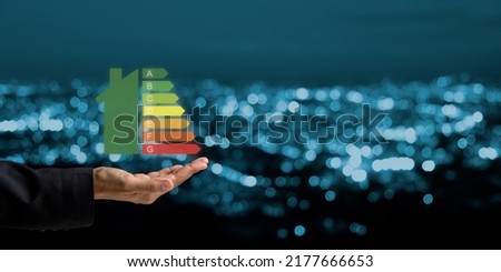 Person hand and house icon with energy efficiency scale image on blue bokeh background, Concept of ecological and bio energetic house. Energy class.