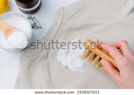 A person hand using a small brush rubbing powder baking soda on a yellow stain on clothing or upholstery. DIY cleaning method using natural products to remove stains. top view. High quality photo