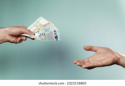 A person handing money to another person. Hands are exchanging euro money. Close-up of hands handling money. 50 euro and 20 euro bills. High-quality photo. Blue, green background.