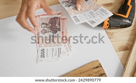 A person handles icelandic krona on a workbench, hinting at a transaction or financial topic in a work setting.