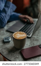 Person hands using a laptop computer next to a coffee cup and smartphone on a table