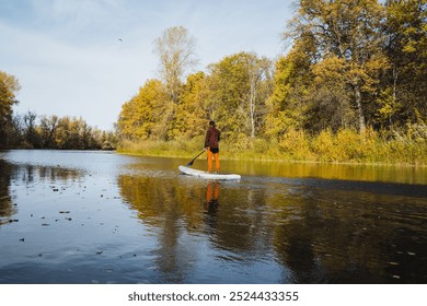 A person is happily enjoying a leisurely paddle board ride across a calm and serene lake, surrounded by breathtaking natural scenery and vibrant lush greenery that enhances the beauty of the location - Powered by Shutterstock