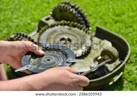 Person has removed the knives from the robotic lawnmower and is holding them in his hand.Robot lawn mower upside down.