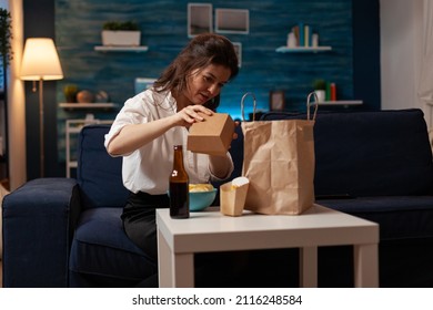 Person Having Burger Junk Food Meal Delivered At Home And Bottled Beer Sitting On Sofa. Woman In Living Room Preparing For Couch Dinner Unboxing Delicious Hamburger From Takeaway Paper Bag.