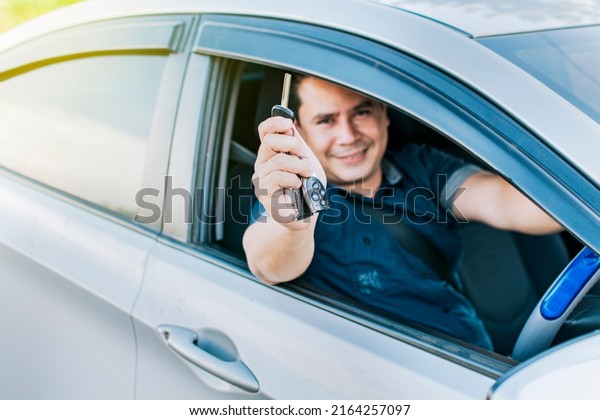 Person in his vehicle showing his\
car keys, A man in his vehicle showing his new car keys, a happy\
guy showing the keys of a new car, vehicle rental\
concept