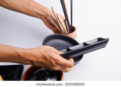 A person is holding a black tray with a spoon and a bowl of chopsticks. The person is also holding a cell phone. Concept of busyness and multitasking - Powered by Shutterstock