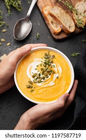 Person Holding Bowl Of Pumpkin Soup Over Black Concrete Background, Top View