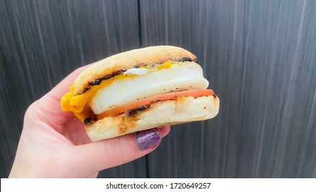 Person Holding Breakfast Sandwich With Egg Ham Bacon And Cheese On Toasted English Muffin Held In Hand
