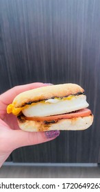 Person Holding Breakfast Sandwich With Egg Ham Bacon And Cheese On Toasted English Muffin Held In Hand
