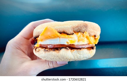 Person Holding Breakfast Sandwich With Egg Ham Bacon And Cheese On Toasted English Muffin