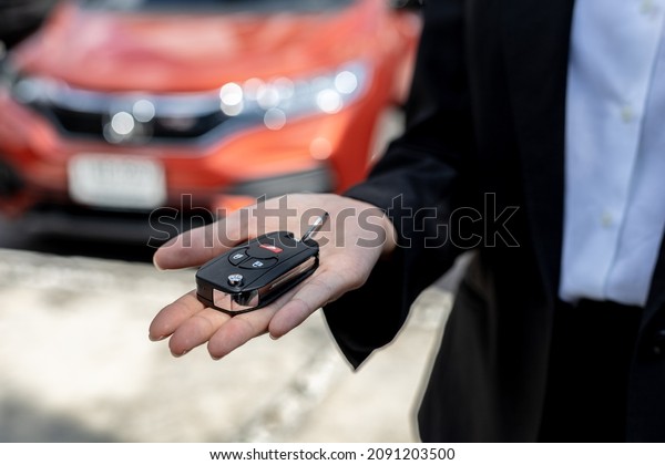 A\
person holding a car key, a female car rental company employee is\
about to deliver the car to a customer who has signed a rental\
contract and paid the deposit. Car rental\
concept.