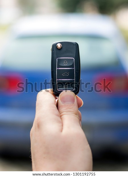 A person holding car key (remote control) in\
hands on blur blue car\
background.