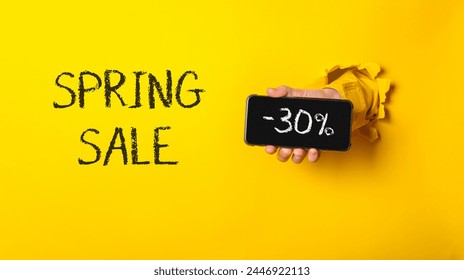 A person holding a cell phone with the words Spring Sale written on it. The phone is being held up to reveal a black sign with the words 30 off - Powered by Shutterstock