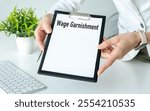 A person holding a clipboard with the word Wage Garnishment written on it. The clipboard is black and white