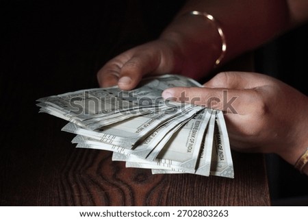 A person holding and counting a stack of Indian Rupee banknotes