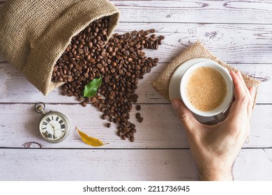 Person Holding Cup Of Espresso Near Coffee Beans And Jute Sack - Time For Breakfast