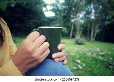 Person Holding Cup Of Tea Or Coffee In Hands. Woman With Glass Of Water In Hand. On Green Nature Park Background. Relax And Breaking Time Concept.