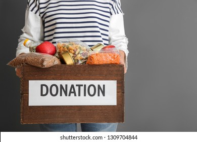 Person Holding Donation Box With Food On Gray Background, Closeup