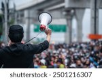 A person holding a megaphone addresses a large crowd during a protest, symbolizing activism, leadership, and public demonstrations.