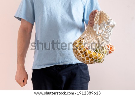 person holding a mesh bag with fresh raw food fruits and vegetables, eco friendly zero waste conversation
