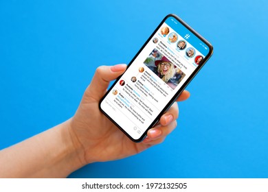 Person holding mobile phone in hand on blue background with sample social media microblogging app on the screen