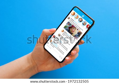 Person holding mobile phone in hand on blue background with sample social media microblogging app on the screen
