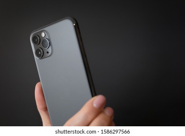 Person holding modern smartphone with triple-lens camera against dark background