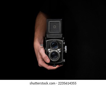 Person holding an old analog camera on a black isolated background.