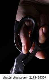 Person Holding An Old Scissors On A Black Background
