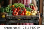 A person holding an open box of fresh vegetables and fruits, including tomatoes, lettuce, beets, lemons, asparagus, carrots, potatoes, green beans in the kitchen door.